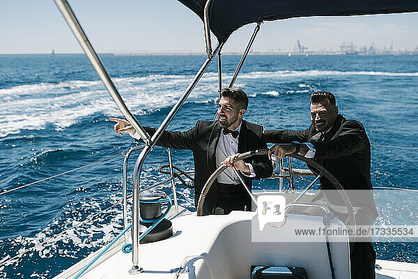 Smiling man pointing by male friend on yacht during sunny day