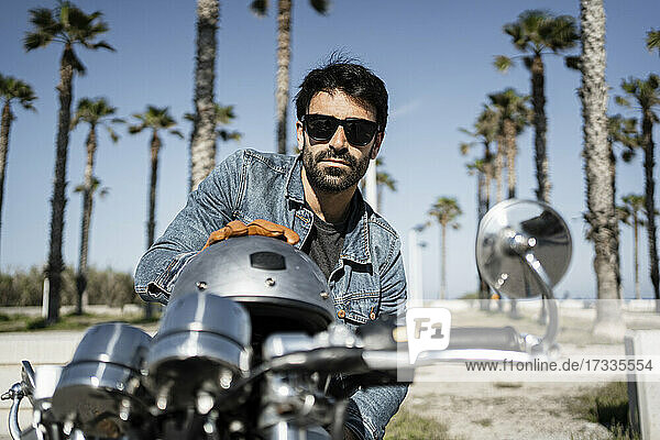 Hübscher junger Mann mit Helm auf einem Motorrad sitzend an einem sonnigen Tag