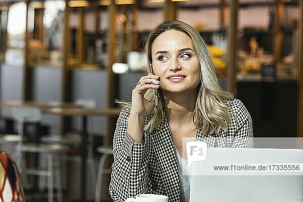 Beautiful female professional talking on smart phone while sitting in cafe