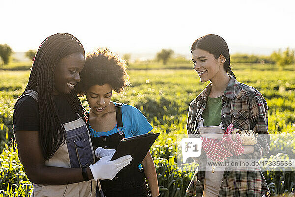 Mother and daughter discussing over digital tablet while standing by female colleague at farm