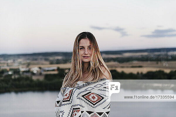 Schöne junge blonde Frau in Decke eingewickelt bei Sonnenuntergang