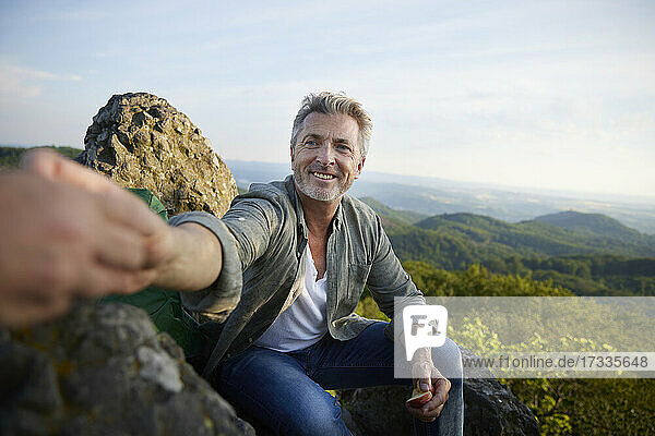 Lächelnder Mann gibt einer Freundin einen Apfel  während er auf einem Berg sitzt