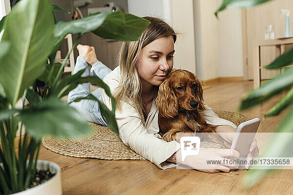 Young woman with Cocker Spaniel using smart phone while lying on floor at home