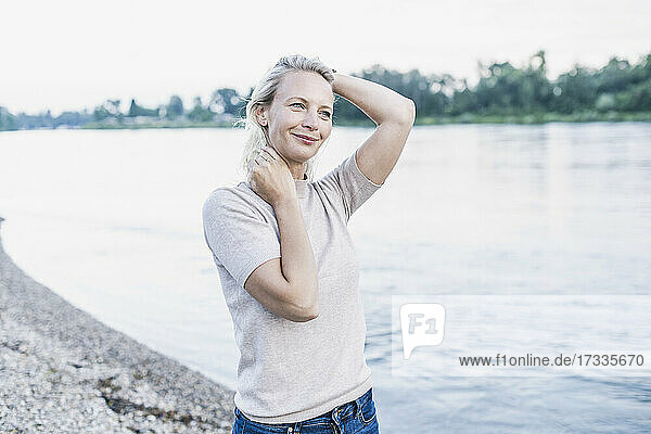 Blonde Frau mit Hand im Haar steht am Flussufer