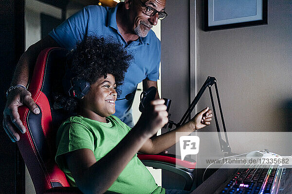 Fröhlicher Junge  der mit seinem Großvater den Sieg feiert  während er zu Hause ein Videospiel spielt