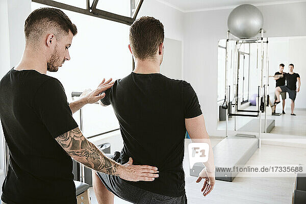 Male instructor providing support to man while exercising at pilates studio