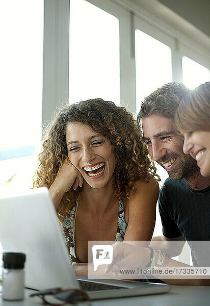 Glückliche männliche und weibliche Freunde teilen sich einen Laptop im Restaurant