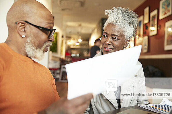 Senior female colleague looking at businessman holding document in restaurant