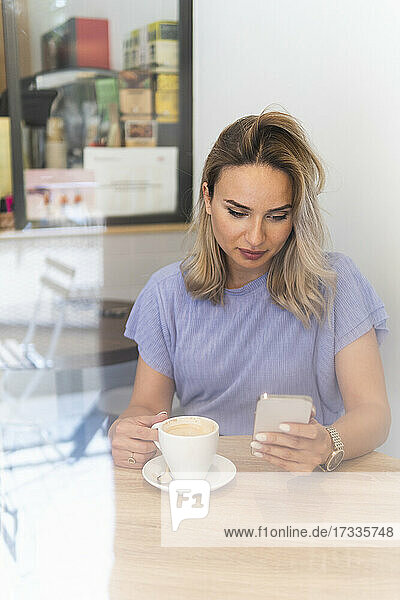 Frau  die ihr Smartphone benutzt  während sie in einem Geschäft Kaffee trinkt