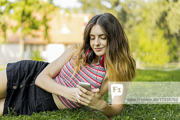 Lächelnde junge Frau  die ein Smartphone benutzt  während sie im Park im Gras liegt