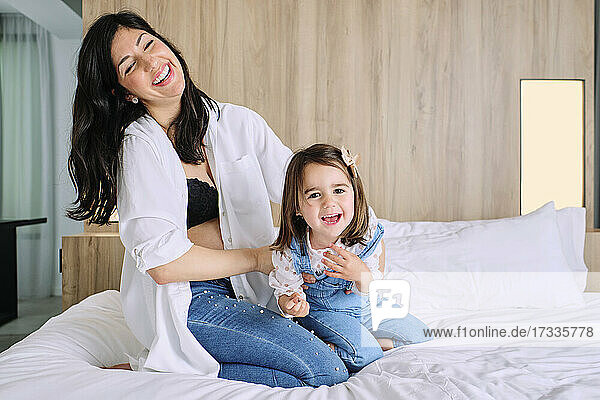 Happy pregnant mother playing with daughter on bed at home