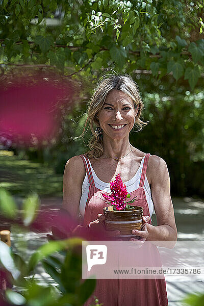 Lächelnde reife Frau stehend mit Blumentopf im Hinterhof