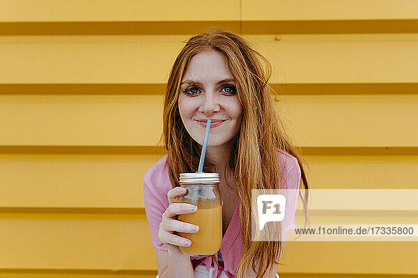 Lächelnde Frau mit Smoothie vor einer gelben Wand