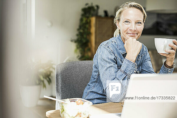 Lächelnde Geschäftsfrau mit Kaffeetasse im Heimbüro