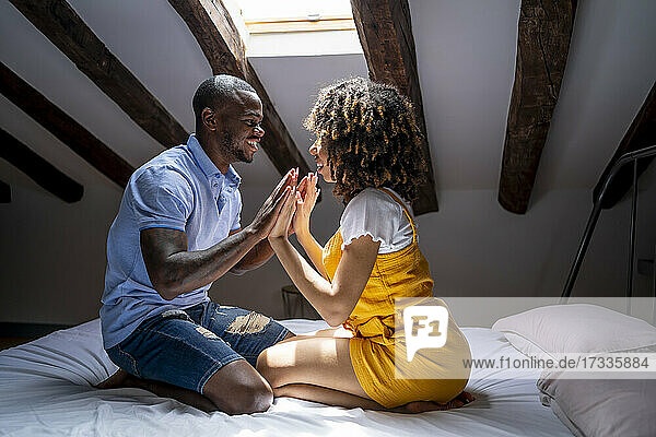 Romantic couple touching hands while sitting on bed in attic at home