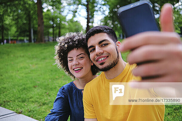 Glückliches junges Paar nimmt Selfie durch Smartphone sitzen im Park