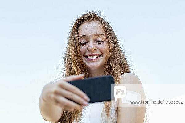 Schöne weibliche Freiberufler unter selfie durch Handy während Himmel im Hintergrund
