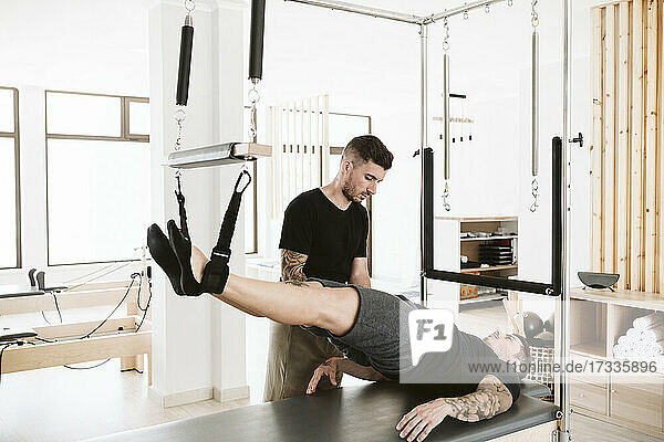 Male instructor teaching pilates exercise to man in studio