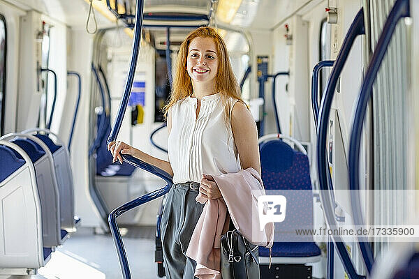 Smiling young businesswoman carrying bag and jacket in train