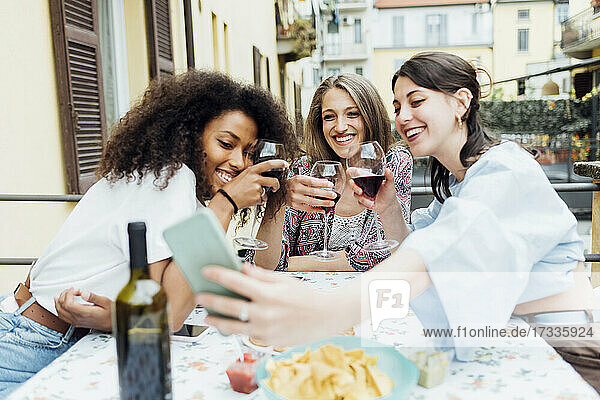 Lächelnde Freunde mit Weingläsern machen ein Selfie mit ihrem Handy auf der Terrasse bei einem geselligen Beisammensein