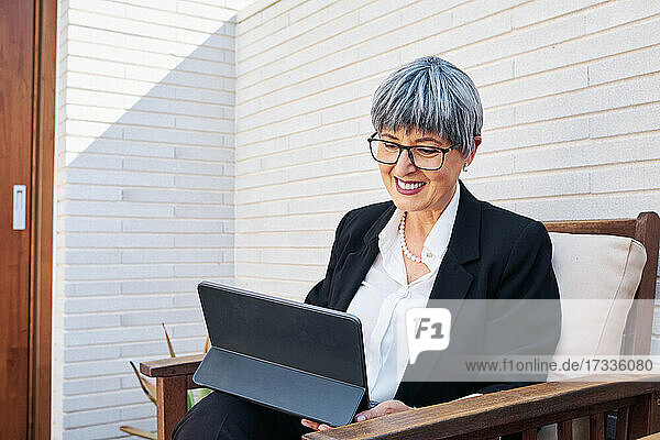 Reife Geschäftsfrau mit kurzen grauen Haaren  die ein digitales Tablet im Hinterhof benutzt
