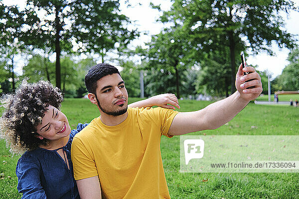 Young man taking selfie with girlfriend through smart phone while sitting at park
