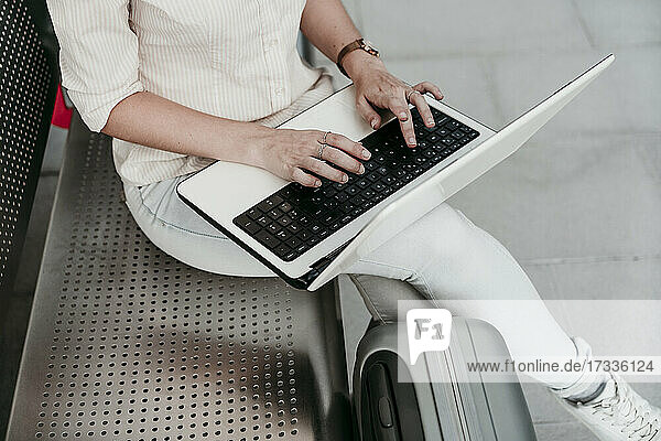 Junge Frau mit Laptop auf einer Bank am Bahnhof sitzend