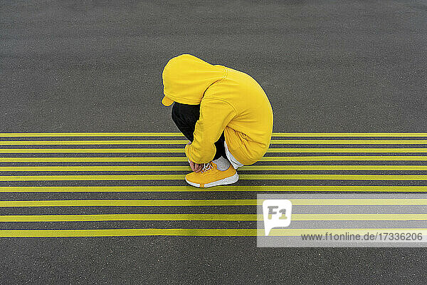 Deprimierter Junge kauert auf gestreiften gelben Straßenmarkierungen