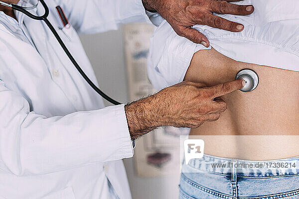 Männlicher Arzt  der in einer Klinik eine Patientin durch ein Stethoskop untersucht