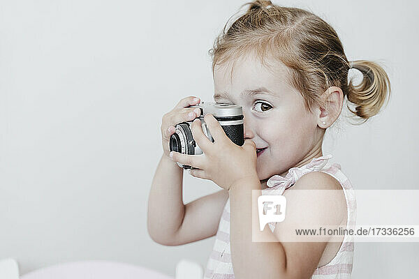 Nettes Mädchen hält Spielzeugkamera vor weißem Hintergrund