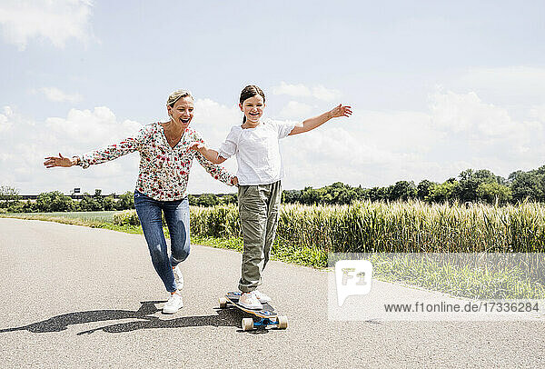 Mother helping daughter on skateboard during sunny day