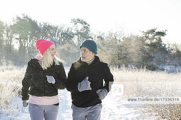 Active senior couple looking at each other while jogging on snow