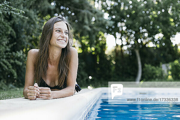 Glückliche Frau schaut weg  während sie am Swimmingpool liegt