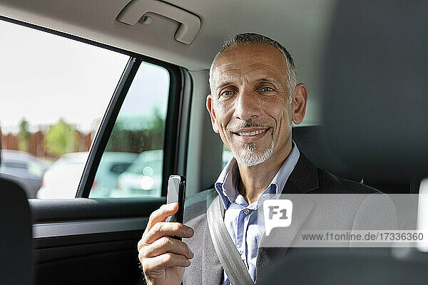 Männlicher Geschäftsmann hält sein Smartphone im Auto sitzend