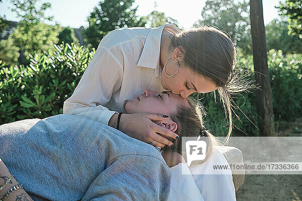Frau küsst Freundin auf die Stirn  während sie im Park sitzt