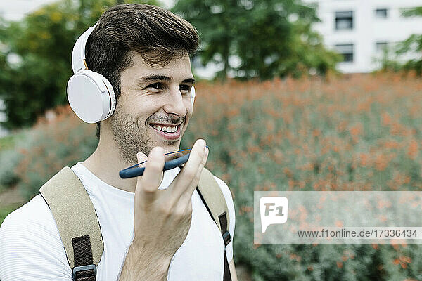 Lächelnder junger Mann  der eine Sprachnachricht über ein Mobiltelefon an eine Wiese sendet