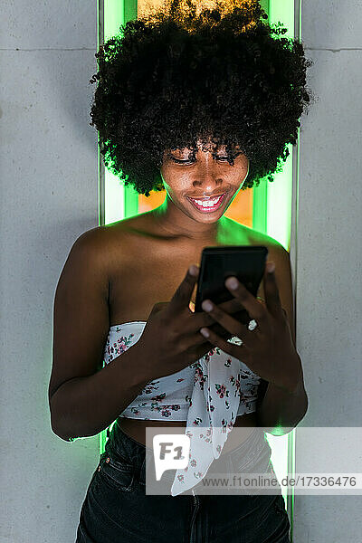 Lächelnde Afro-Frau mit Mobiltelefon vor Neonlicht