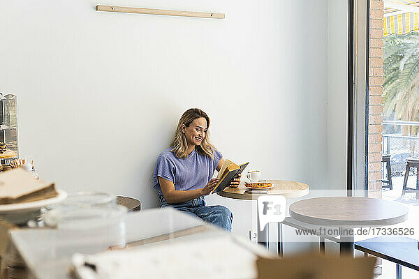 Lächelnde junge Frau liest ein Buch  während sie an einem Tisch in einem Café sitzt