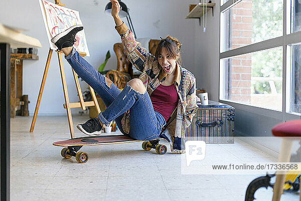 Fröhliche junge Frau auf einem Skateboard im Atelier eines Künstlers