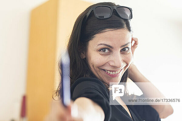 Glückliche Geschäftsfrau mit Sonnenbrille  die im Büro stehend einen Stift gibt