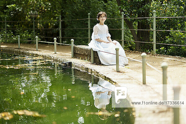 Mädchen im weißen Kleid sitzt auf einem Felsen am Teich im Garten