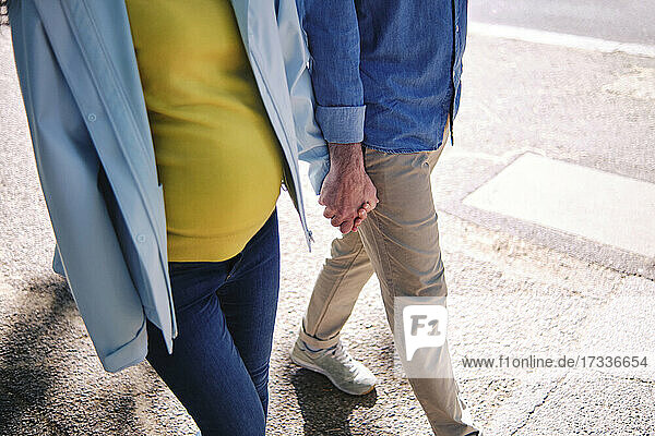 Schwangere Frau hält die Hand ihres Mannes beim Gehen auf der Straße