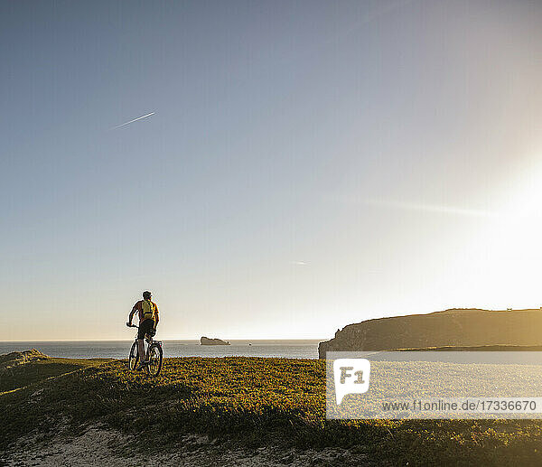 Männlicher Sportler auf einem elektrischen Mountainbike auf einer Wiese bei Sonnenuntergang