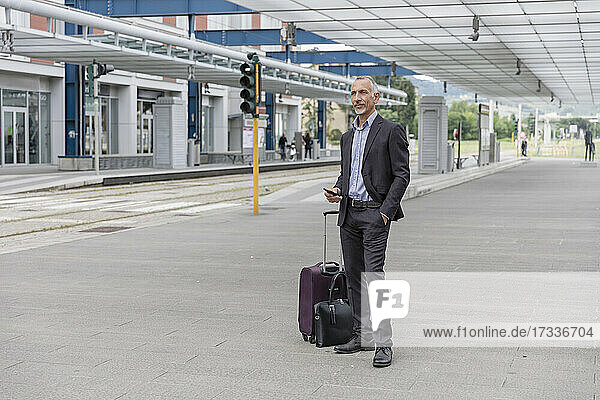 Businessman with luggage waiting for train at railroad station