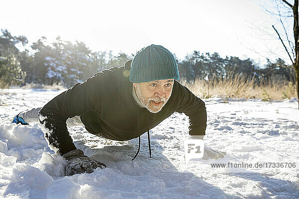Engagierter älterer Mann macht Liegestütze im Schnee