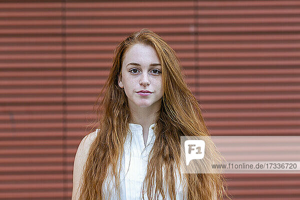 Young redhead businesswoman standing in front of wall