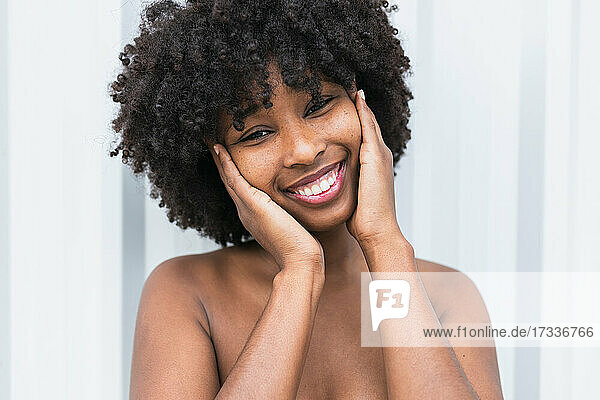 Afro woman with head in hands smiling in front of wall
