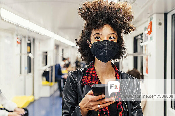 Frau mit Gesichtsmaske hält Mobiltelefon in U-Bahn-Zug