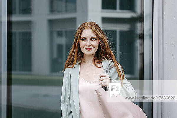 Beautiful redhead businesswoman with purse in front of window