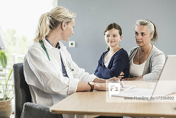 Kinderarzt und Frau im Gespräch beim Sitzen in der Arztpraxis